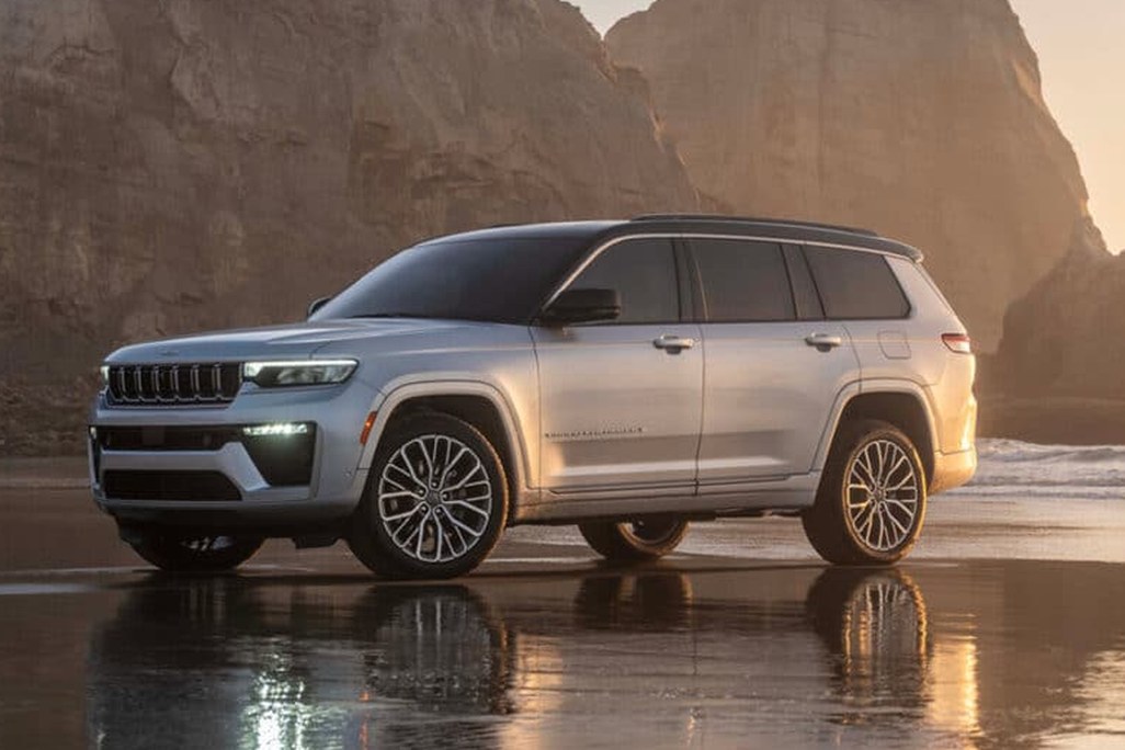Silver SUV parked on a reflective wet beach, with rocky cliffs in the background at sunset.