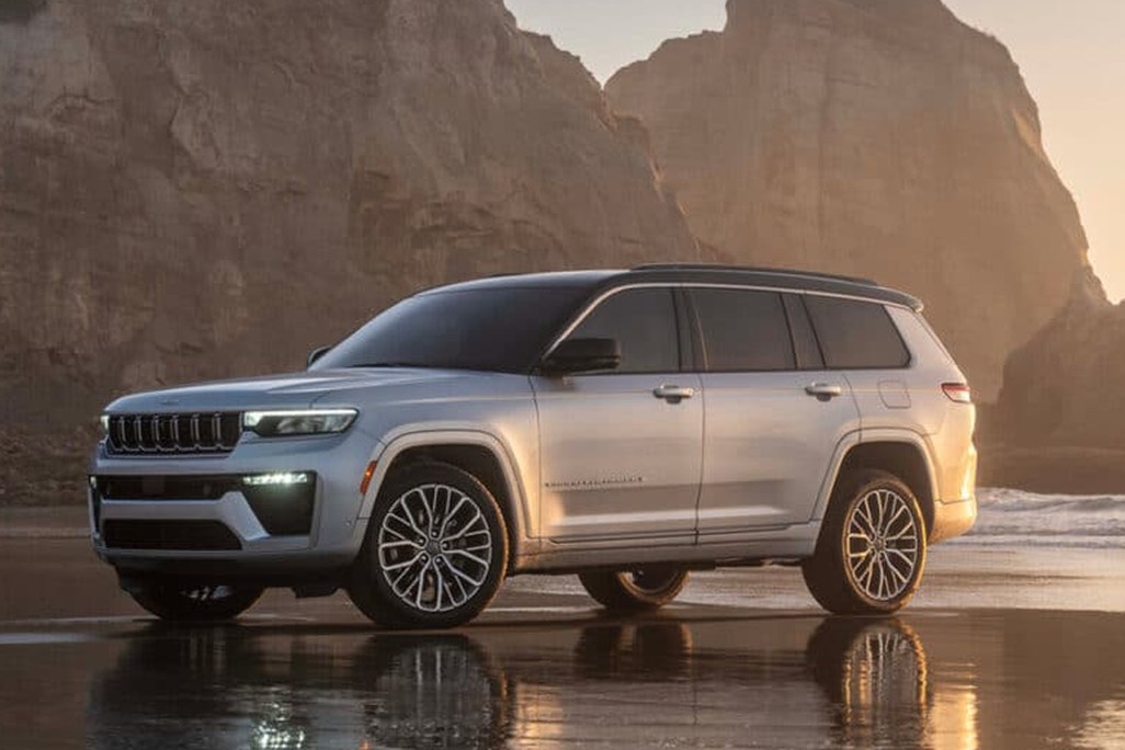 A silver SUV parked on a reflective beach at sunset, with towering cliffs in the background.