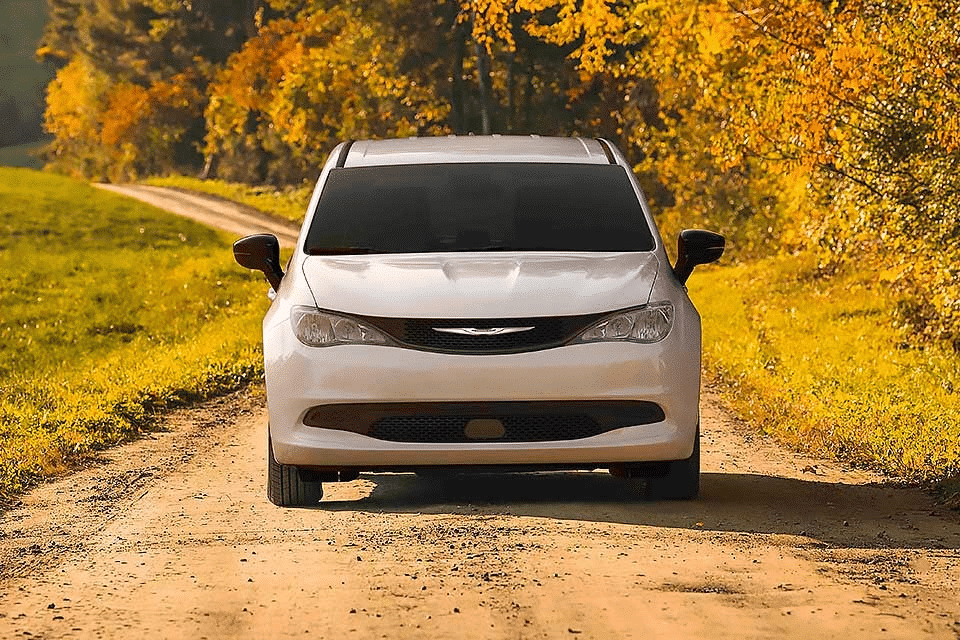 White car driving on a rural dirt road with vibrant autumn foliage in the background.